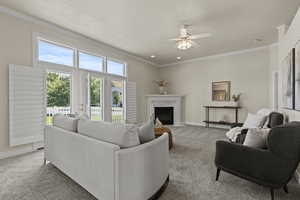 Carpeted living area featuring a high end fireplace, a textured ceiling, ornamental molding, and ceiling fan