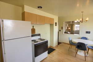 Kitchen featuring freestanding refrigerator, electric range, light wood finished floors, a chandelier, and hanging light fixtures