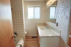 Bathroom with wallpapered walls, vanity, shower / tub combination, and wood finished floors