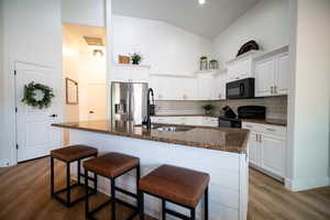 Kitchen with black appliances, a kitchen bar, high vaulted ceiling, and white cabinets