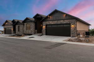 View of front of property with an attached garage, stone siding, concrete driveway, and board and batten siding