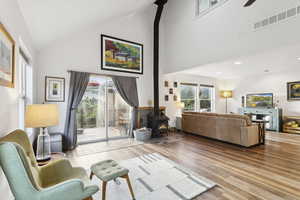Living room with a wood stove, high vaulted ceiling, wood finished floors, and ceiling fan
