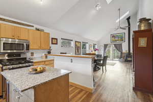 Kitchen featuring a center island, stainless steel appliances, a wood stove, wood finished floors, and high vaulted ceiling