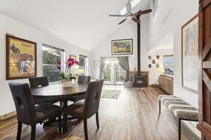 Dining area with a wood stove, wood finished floors, high vaulted ceiling, and ceiling fan
