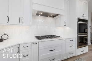 Kitchen with stainless steel appliances, white cabinets, custom exhaust hood, tasteful backsplash, and light wood-type flooring