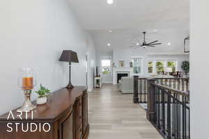 Hall with vaulted ceiling, an upstairs landing, light wood finished floors, and recessed lighting