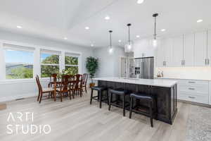 Kitchen with recessed lighting, a center island with sink, light countertops, high quality fridge, and light wood-style floors