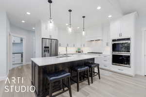 Kitchen featuring appliances with stainless steel finishes, light countertops, an island with sink, light wood-type flooring, and recessed lighting
