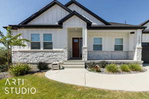 View of front of property featuring stone siding, board and batten siding, an attached garage, a porch, and a front yard