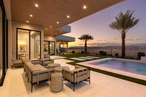 Pool at dusk with a patio area, an outdoor hangout area, and a fenced backyard
