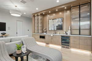 Indoor wet bar with beverage cooler, recessed lighting, light wood finished floors, and hanging light fixtures