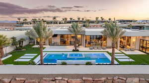Back of house at dusk featuring stucco siding, a putting green, a patio, a fenced backyard, and a pool with connected hot tub