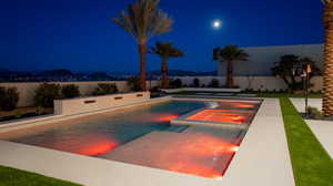 Pool at night with a mountain view, a pool with connected hot tub, and a patio