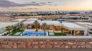 Back of house at dusk with a fenced backyard, a patio, an outdoor pool, a mountain view, and stucco siding