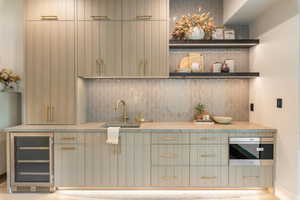 Bar area featuring beverage cooler, backsplash, light wood-style floors, and stainless steel microwave