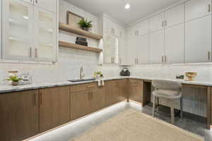 Kitchen with light stone countertops, backsplash, glass insert cabinets, open shelves, and recessed lighting