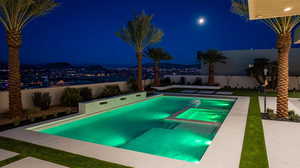 Pool at night featuring a pool with connected hot tub