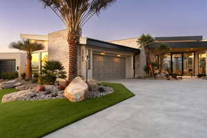 Contemporary house with a garage, concrete driveway, stucco siding, and a lawn