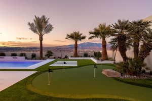 Pool at dusk with an area to practice putting, a fenced backyard, a mountain view, and a patio area
