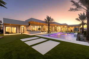 Pool at dusk featuring a putting green, a patio area, an outdoor pool, and a yard