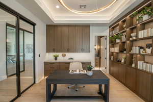 Home office featuring a tray ceiling and light wood-type flooring