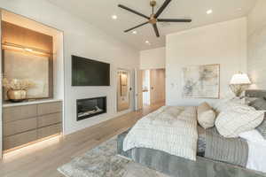 Bedroom with a glass covered fireplace, light wood finished floors, recessed lighting, a high ceiling, and a ceiling fan