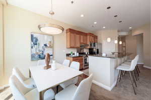 Kitchen with dark countertops, light colored carpet, stainless steel appliances, a kitchen breakfast bar, and recessed lighting