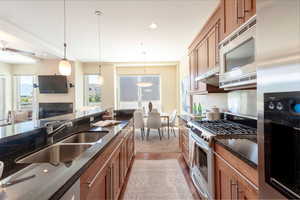 Kitchen with appliances with stainless steel finishes, brown cabinetry, dark stone countertops, hanging light fixtures, and recessed lighting