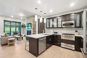 Kitchen with stainless steel appliances, open floor plan, light countertops, a peninsula, and light wood finished floors