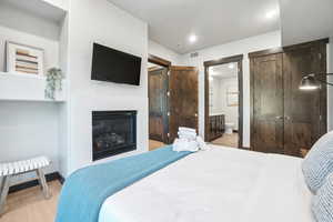 Bedroom featuring light wood-style floors, a glass covered fireplace, ensuite bathroom, and recessed lighting