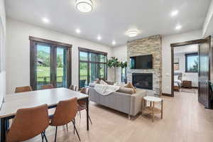 Living area with a stone fireplace, light wood-type flooring, recessed lighting, and french doors