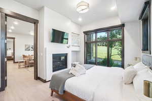Bedroom featuring a glass covered fireplace, light wood-style floors, and recessed lighting