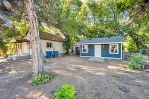 View of front of house with view of scattered trees, an outdoor structure, and a shingled roof