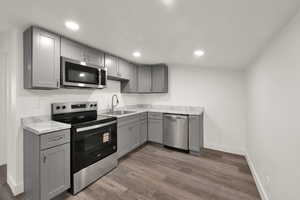 Kitchen featuring gray cabinets, appliances with stainless steel finishes, light countertops, dark wood finished floors, and recessed lighting