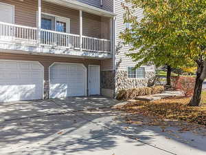 View of front of house featuring driveway, stone siding, an attached garage, and a balcony
