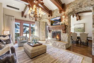 Living area with beam ceiling, a stone fireplace, and a chandelier