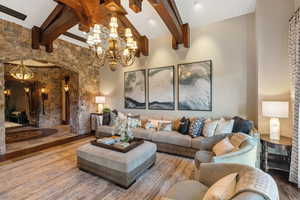 Living area with beam ceiling, wood finished floors, high vaulted ceiling, arched walkways, and a chandelier