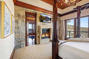 Bedroom featuring a glass covered fireplace, wood ceiling, crown molding, and a chandelier