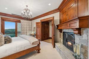 Bedroom with access to outside, crown molding, light colored carpet, a stone fireplace, and a chandelier