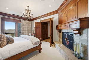 Bedroom with light carpet, a stone fireplace, ornamental molding, access to exterior, and a chandelier