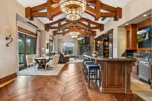 Community bar area with a lit fireplace, high vaulted ceiling, decorative backsplash, a chandelier, and beamed ceiling