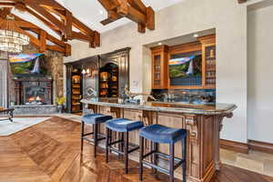 Indoor wet bar with beam ceiling, a stone fireplace, a high ceiling, decorative backsplash, and hanging light fixtures