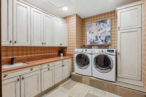 Laundry room with cabinet space, independent washer and dryer, wallpapered walls, stone tile flooring, and recessed lighting