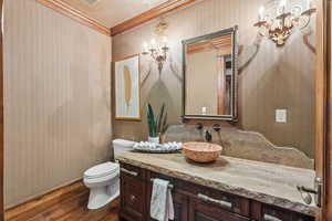 Bathroom with wallpapered walls, ornamental molding, vanity, wood finished floors, and a chandelier