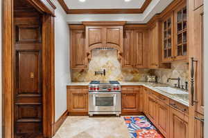 Kitchen with designer range, ornamental molding, brown cabinetry, light stone counters, and glass insert cabinets