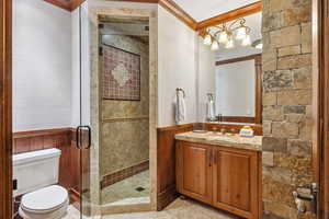 Full bath featuring a stall shower, ornamental molding, vanity, and wainscoting