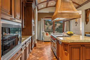Kitchen featuring range with two ovens, island exhaust hood, brown cabinetry, light stone countertops, and a kitchen island