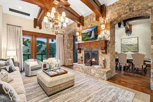 Living area featuring beam ceiling, a fireplace, wood finished floors, and a chandelier