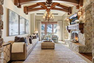 Living area featuring a stone fireplace, a chandelier, and beam ceiling
