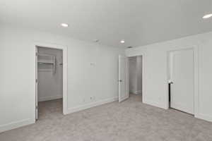 Unfurnished bedroom featuring light colored carpet, a walk in closet, and recessed lighting